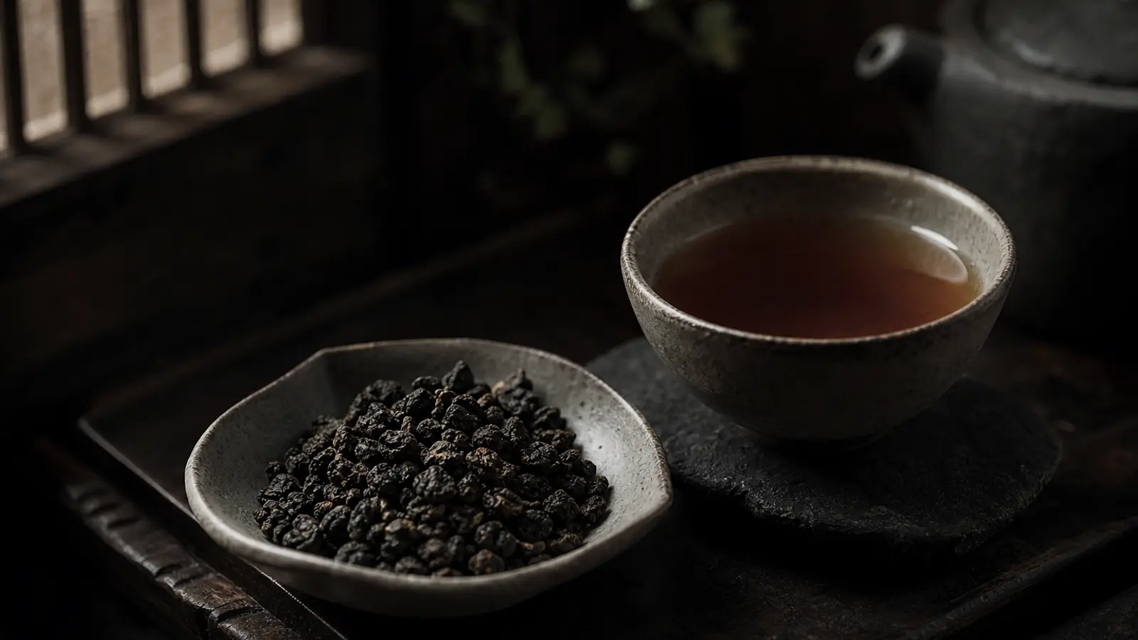 Dark roasted Dong Ding oolong tea pellets in a ceramic dish beside a cup of warm amber liquor in editorial product photography