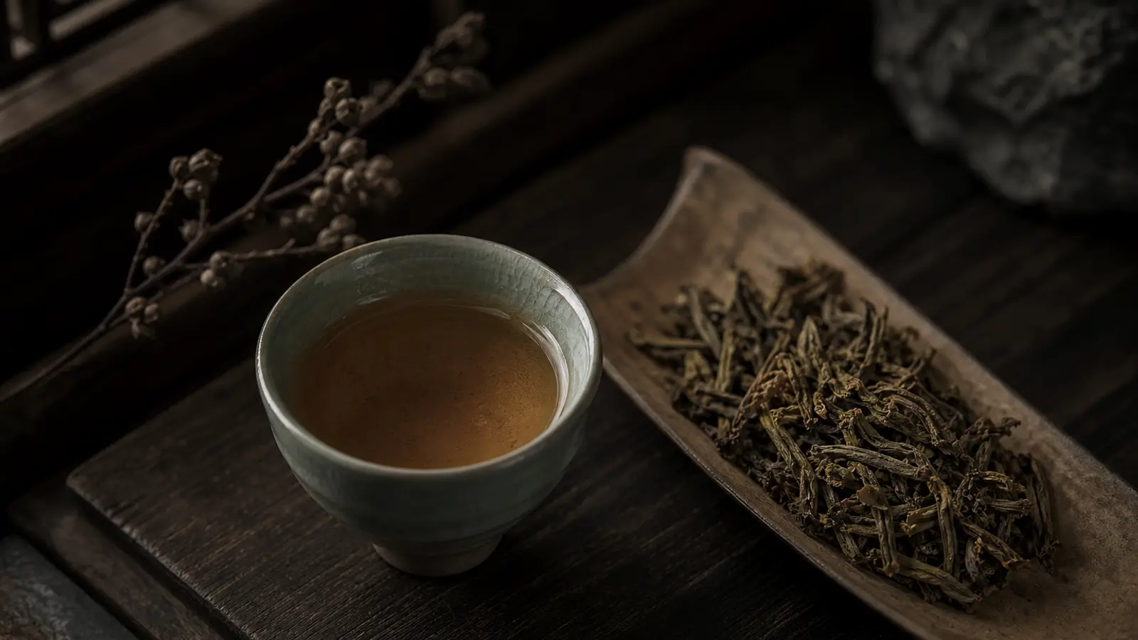 Amber-gold hwangcha tea in a celadon cup beside yellow-gold oxidized leaves on a wooden surface.